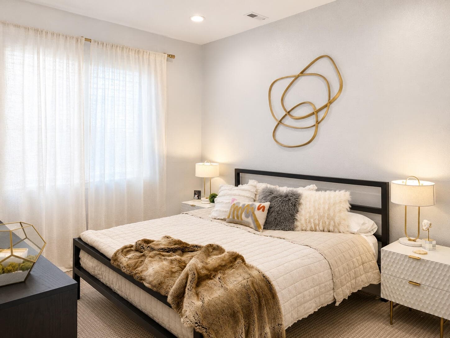 Bright bedroom with a black metal bed, a fur throw and gold ring wall art