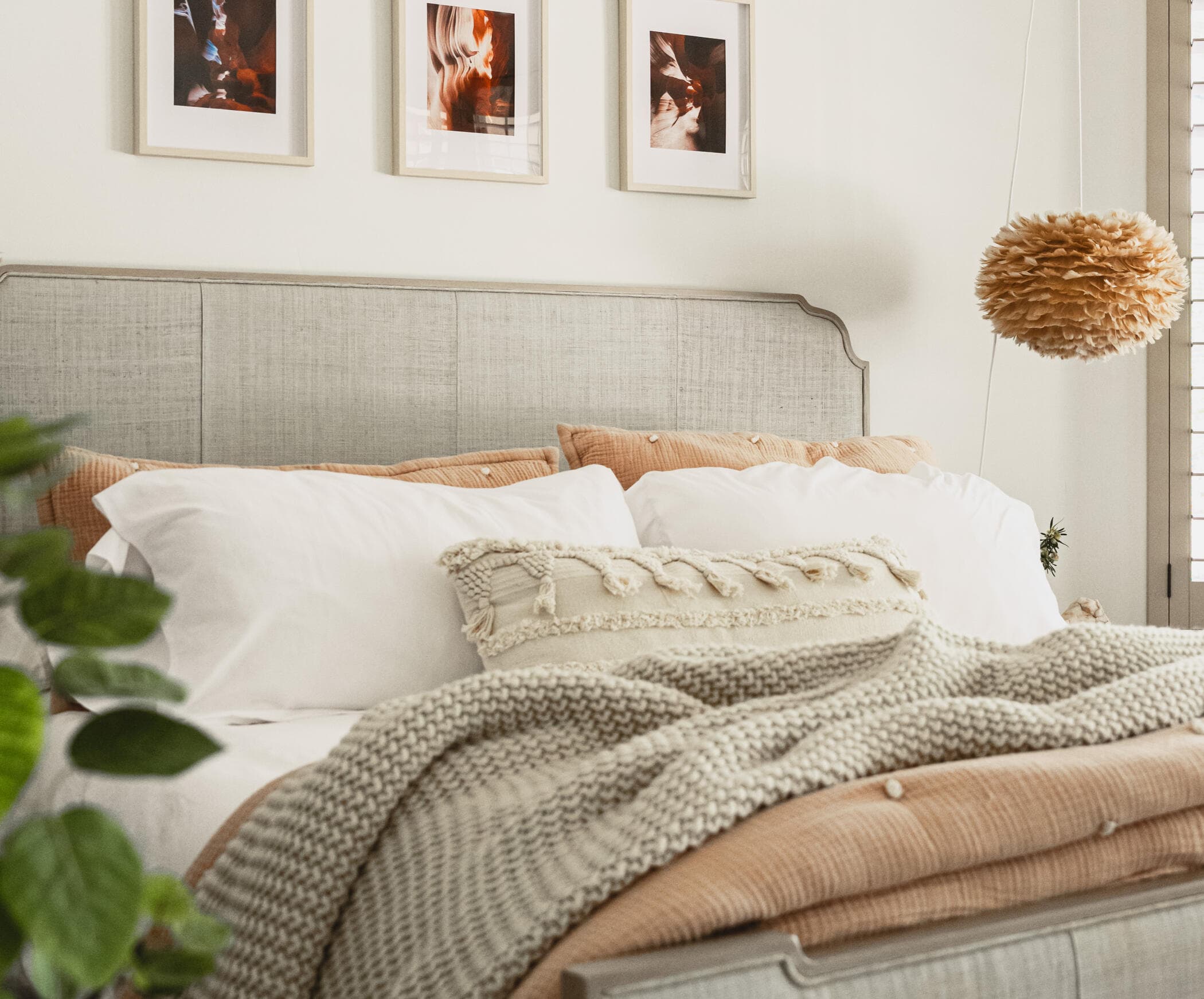 Bedroom with a woven headboard, layered white and terracotta bedding and a feather pendant