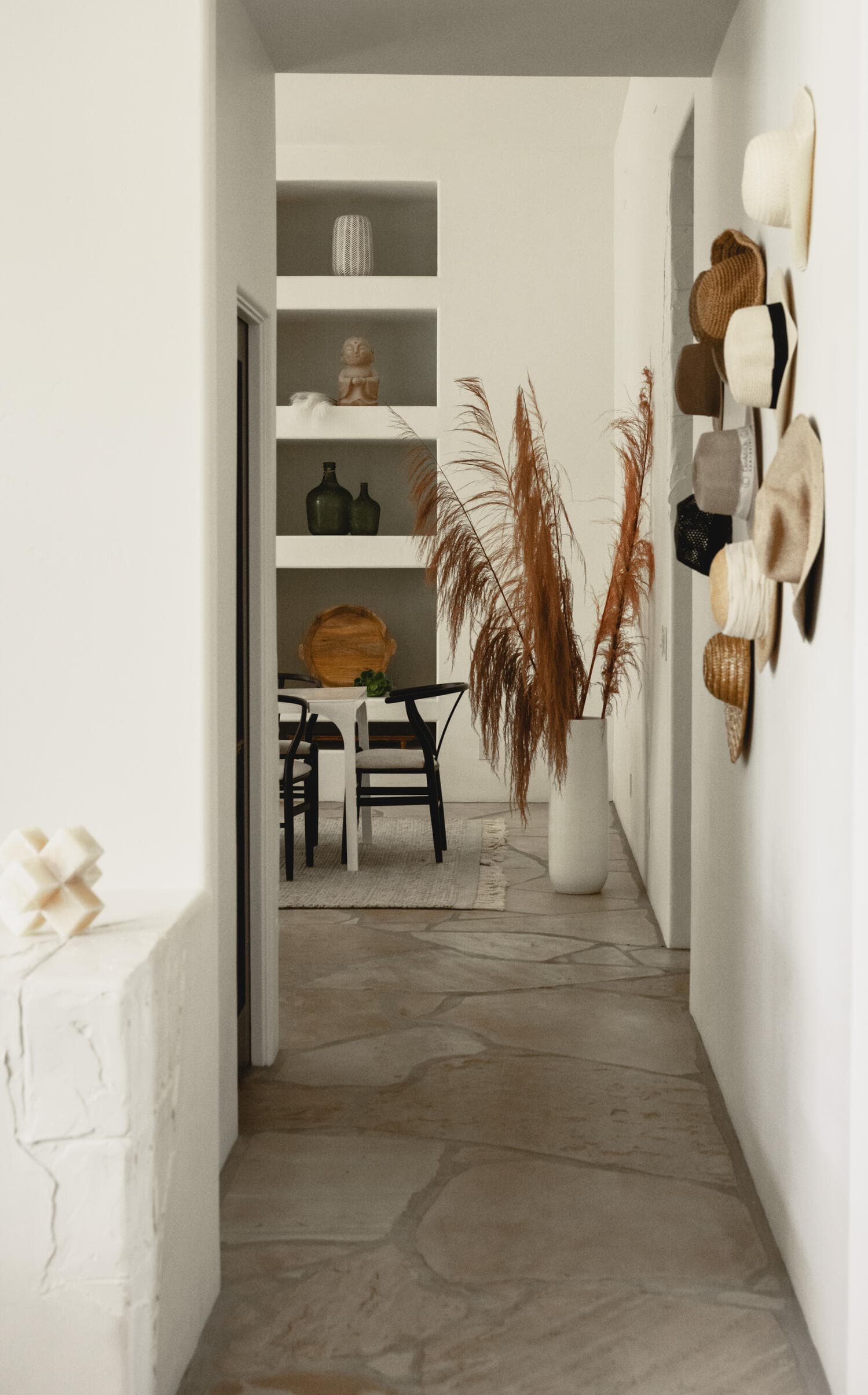 Flagstone hallway with white plaster walls, a wall of woven hats and built-in niches beyond